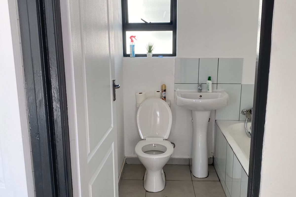 A functional bathroom featuring a pedestal basin, toilet, and bathtub with neutral floor and wall tiling.