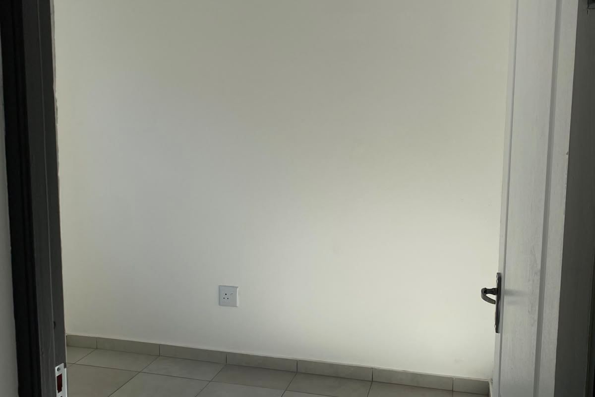 A bright, empty bedroom featuring neutral tiled flooring, a white tongue and groove ceiling with recessed lighting, and a clean, minimalist aesthetic.