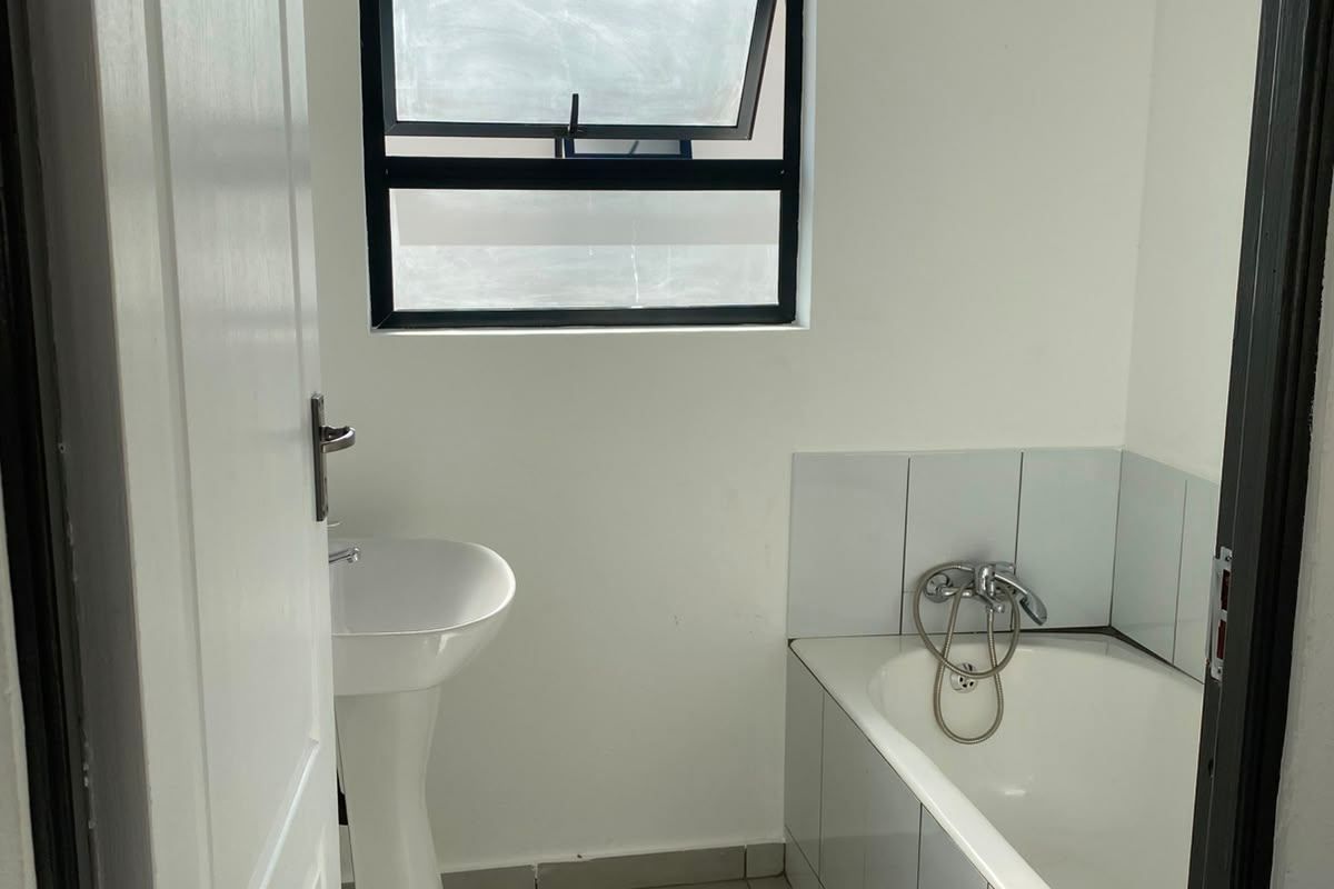 A clean, functional bathroom featuring a pedestal basin, a built-in bathtub with tiled surround, and neutral floor tiling.