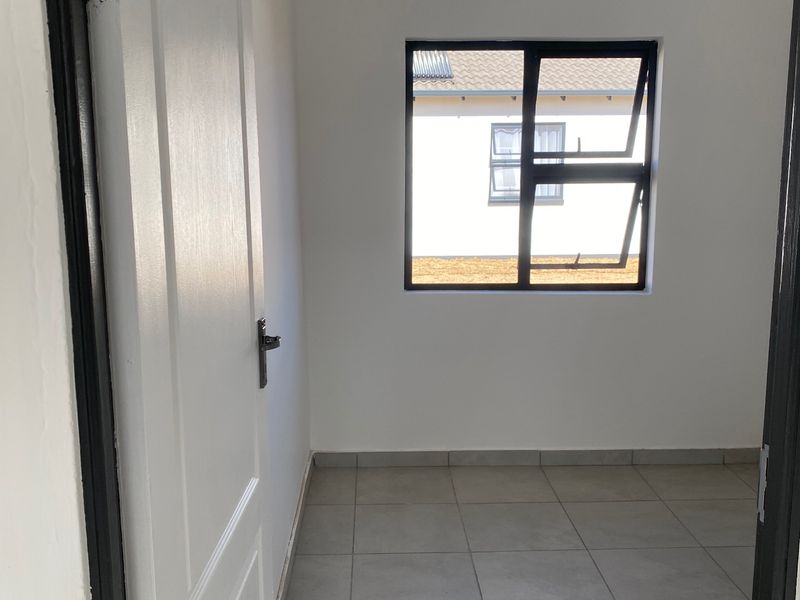 A clean, empty bedroom featuring neutral tiled flooring, a modern aluminium window, and a white panelled door.
