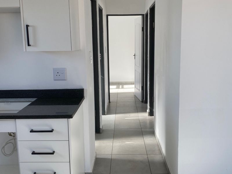 A bright, modern hallway featuring neutral floor tiles, clean white walls, and built-in cabinetry, leading towards additional rooms in the property.