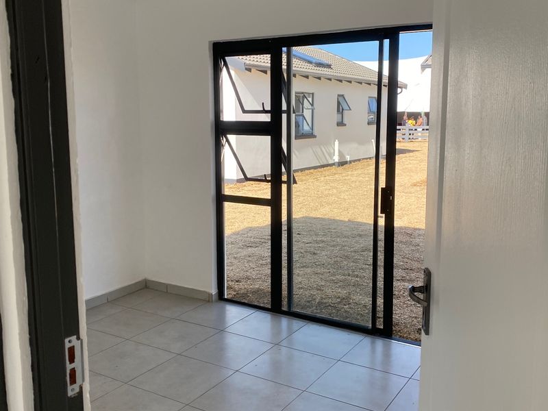 A bright, empty room featuring modern tiled flooring, recessed ceiling lights, and a sliding glass door providing direct access to the rear garden.