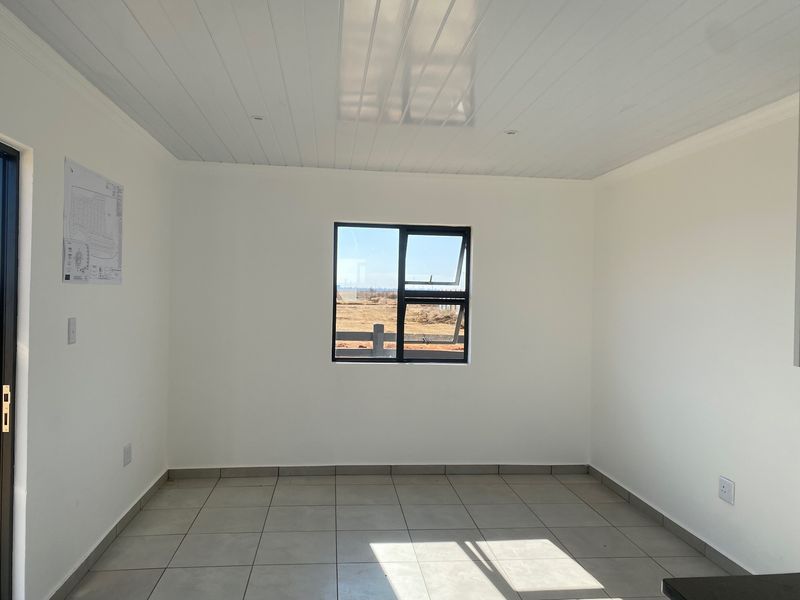 A bright, empty living area featuring neutral tiled flooring, clean white walls, and a modern PVC ceiling with a central window.