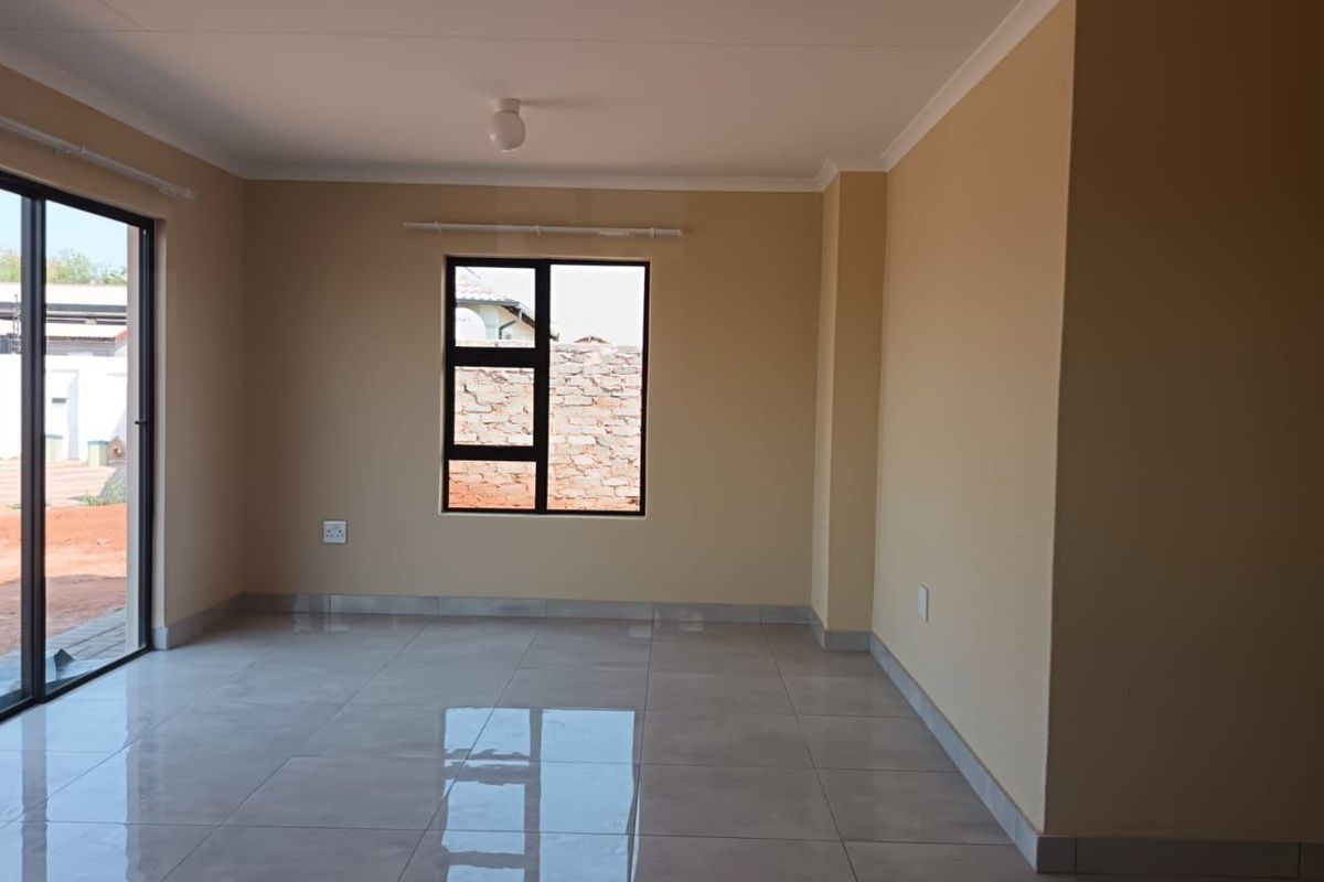 A bright, empty living area featuring neutral walls, large format floor tiles, and a sliding glass door providing access to the exterior.