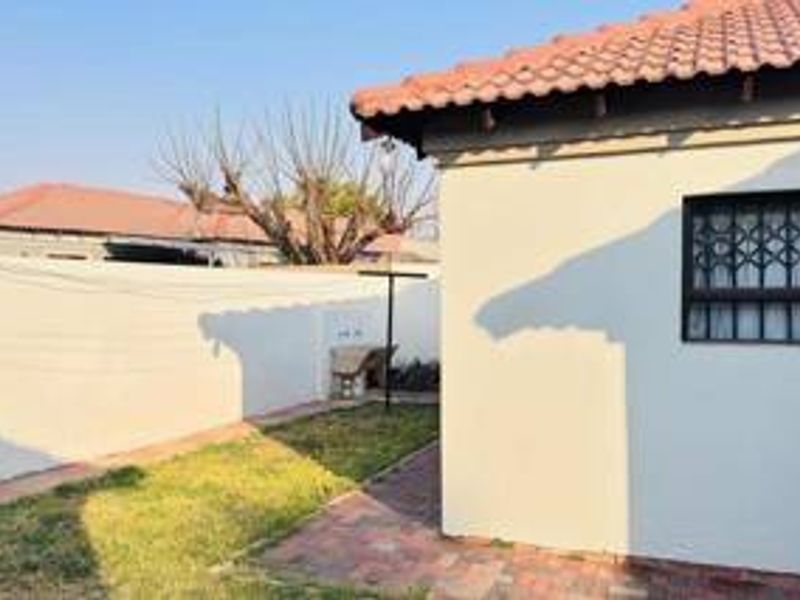 A view of the rear exterior of the house featuring a tiled roof, security bars on the window, and a paved area with a wash basin.