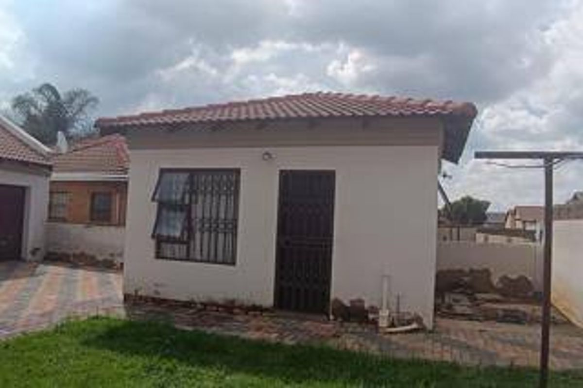Rear view of the property featuring a tiled roof, security-fitted windows and doors, and a paved patio area with an installed washing line.