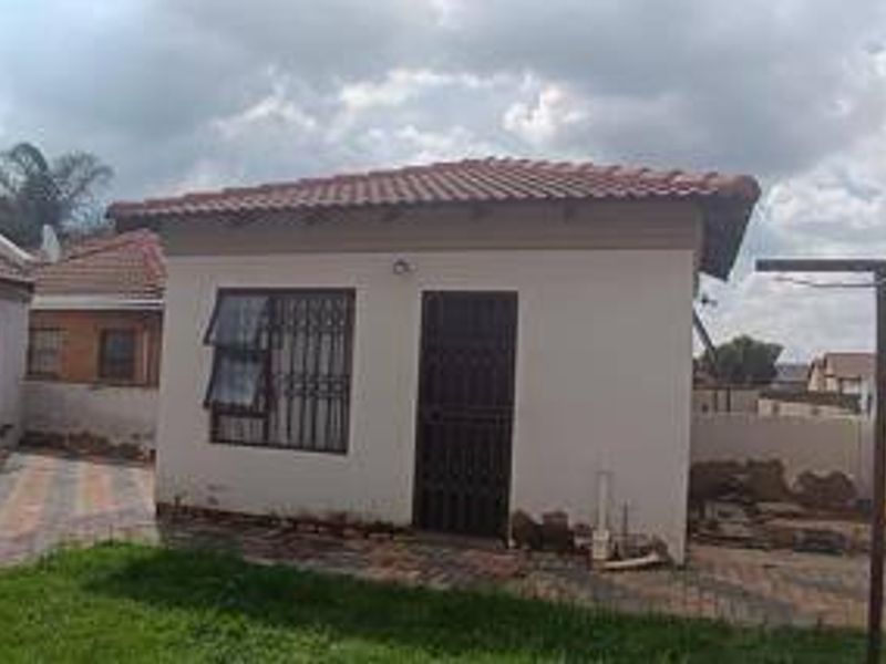 Rear view of the property featuring a tiled roof, security-fitted windows and doors, and a paved patio area with an installed washing line.