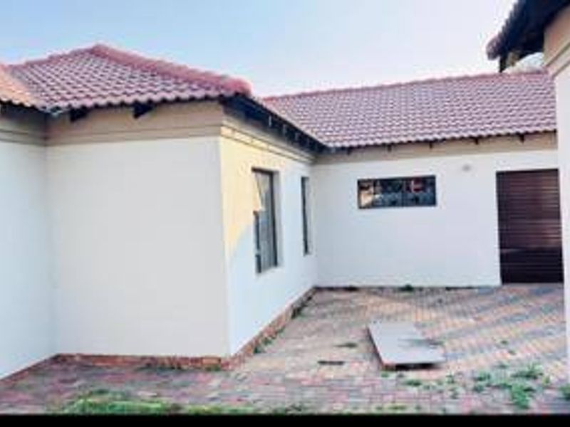 A rear exterior view of the property featuring a paved courtyard area, tiled roofing, and access to the garage.