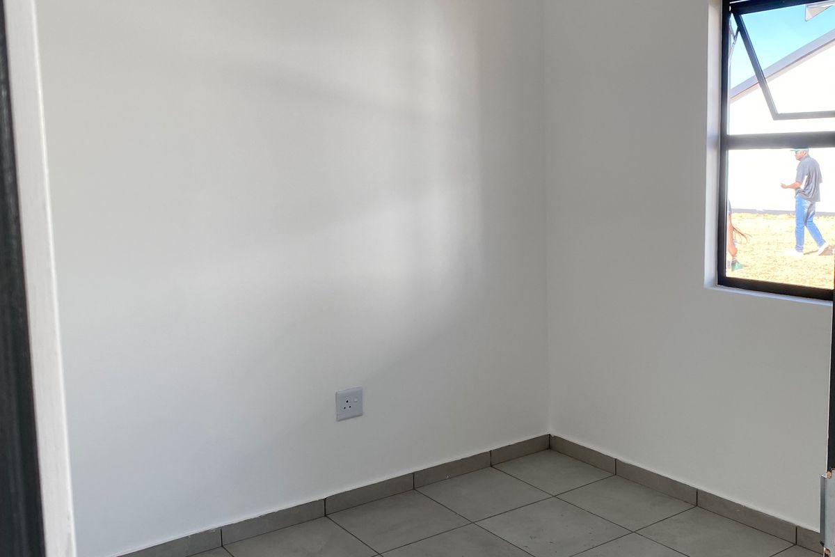 A clean, empty bedroom featuring neutral tiled flooring, a white tongue and groove ceiling, and a modern casement window.