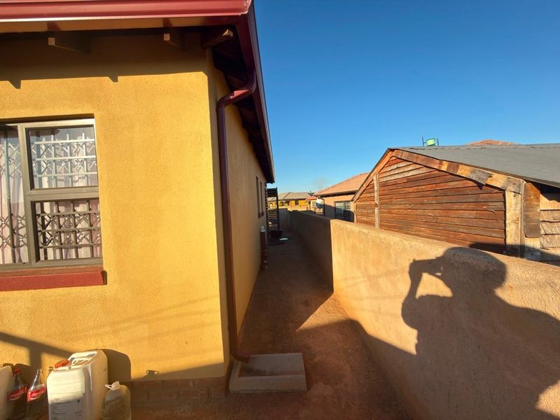 A narrow side passage of the house featuring a yellow rendered wall, security bars on the window, and a boundary wall.