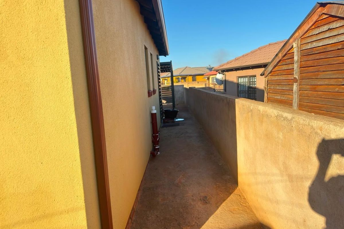 A narrow side passage of the property featuring a concrete pathway, boundary wall, and exterior downpipe.