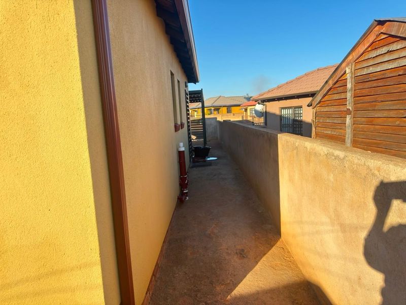 A narrow side passage of the property featuring a concrete pathway, boundary wall, and exterior downpipe.