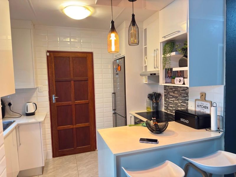 A modern, well-maintained kitchen featuring white cabinetry, subway tile backsplash, stone countertops, and integrated appliances with stylish pendant lighting.