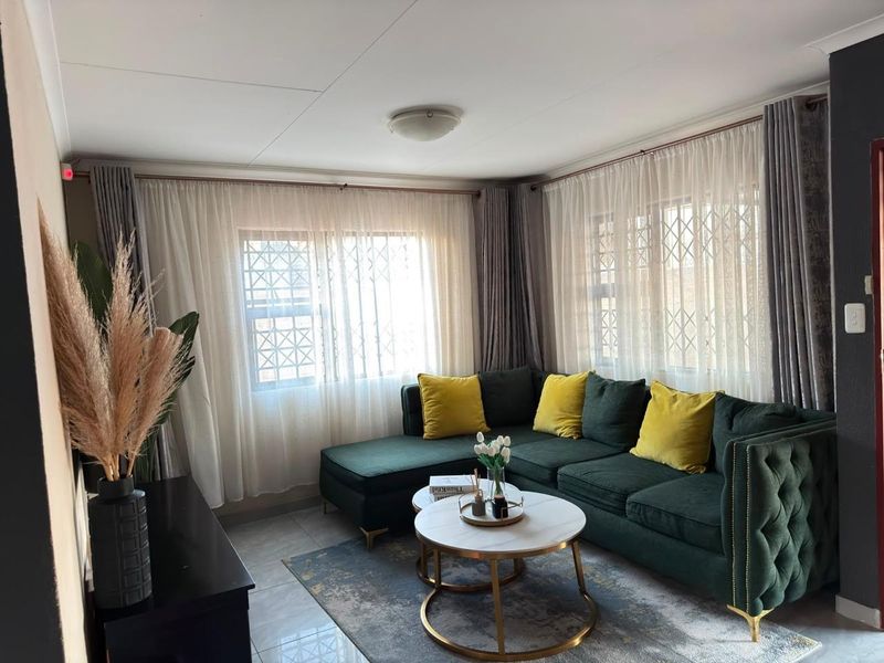A well-maintained living room featuring tiled flooring, large windows with security burglar bars, and neutral wall finishes.