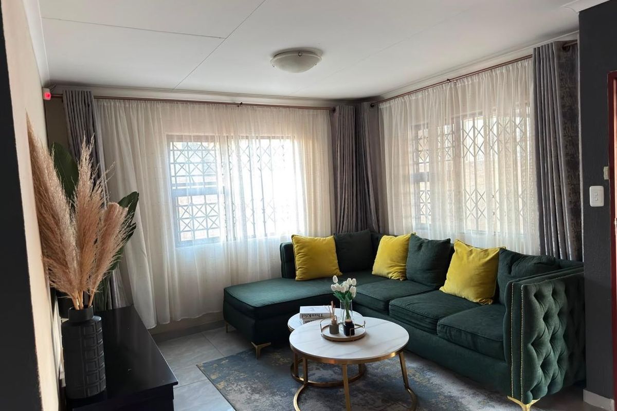 A well-maintained living room featuring tiled flooring, large windows with security burglar bars, and neutral wall finishes.