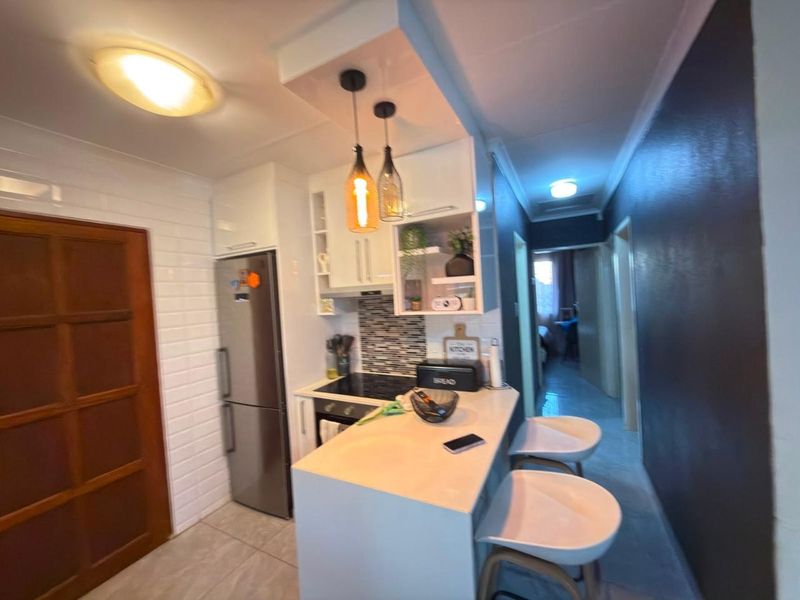 Compact modern kitchen featuring built-in cabinetry, stone countertops, a breakfast bar, and integrated appliances, leading into a hallway.