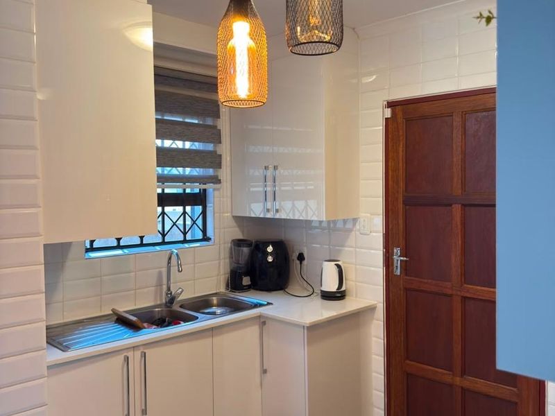 A modern kitchen featuring white high-gloss cabinetry, a stainless steel sink, subway tile backsplash, and stylish pendant lighting.