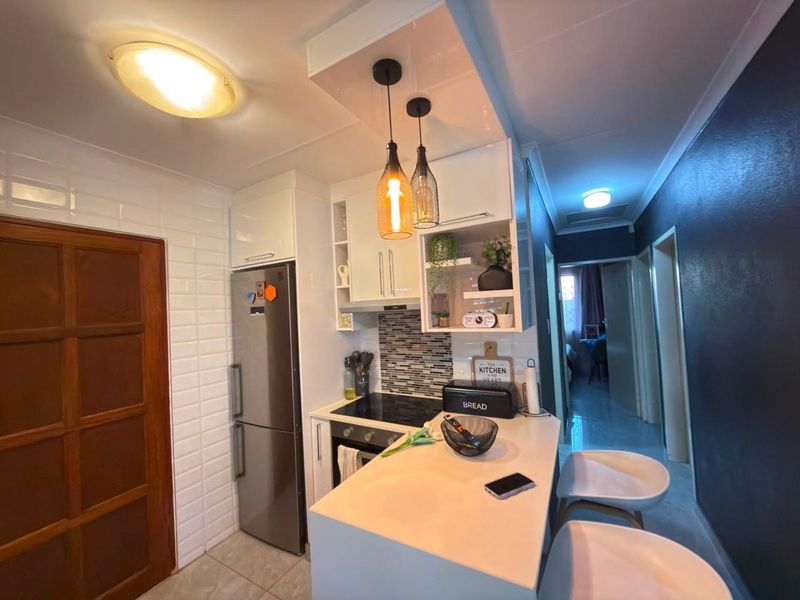 Modern compact kitchen featuring sleek white cabinetry, stone countertops, a built-in electric hob and oven, and stylish pendant lighting.