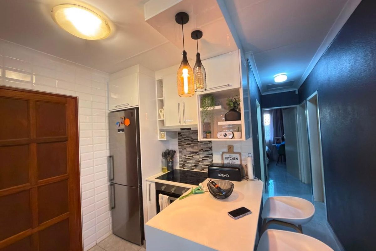 Modern compact kitchen featuring sleek white cabinetry, stone countertops, a built-in electric hob and oven, and stylish pendant lighting.