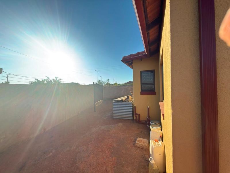 A view of the rear exterior side yard featuring a perimeter wall, downpipe, and tiled roof overhang.