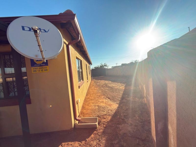 A view of the rear exterior side of the house featuring a satellite dish, security signage, and an unlandscaped yard area.