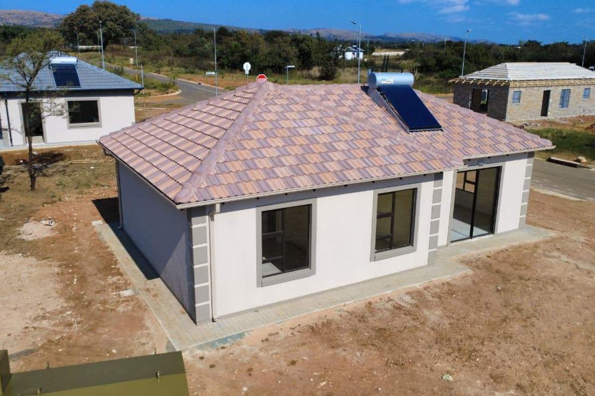 Aerial view of a modern single-story residential house featuring a tiled roof, solar water heating system, and paved perimeter in a developing estate.