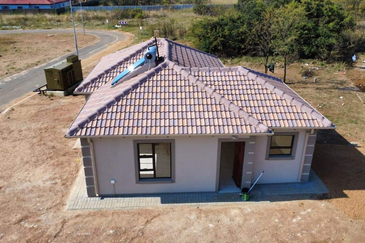 Aerial view of a single-story residential house featuring a tiled roof with an integrated solar water heating system and paved perimeter.