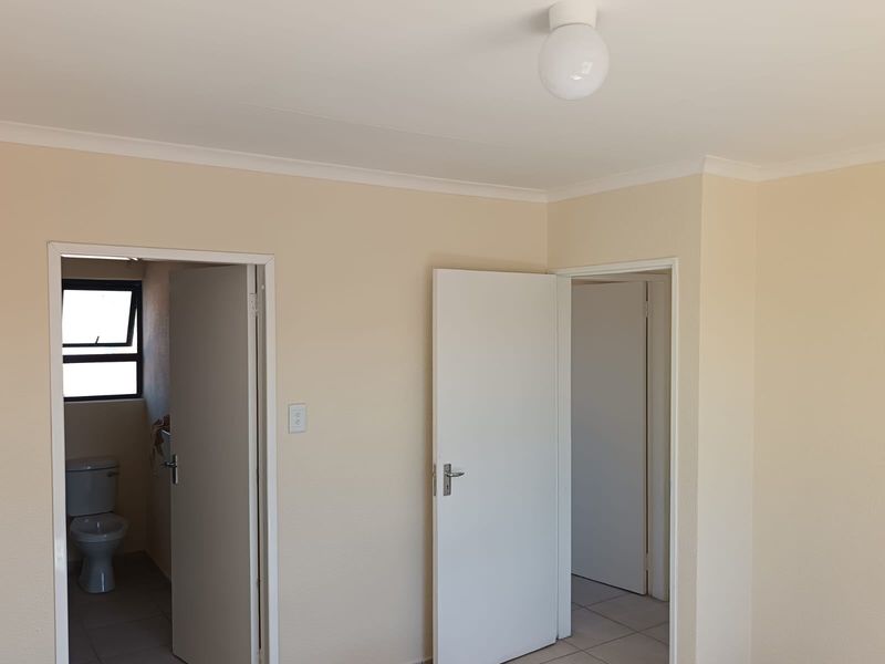 A neutral-toned hallway featuring tiled flooring, coving, and access to adjacent rooms, including a visible bathroom.
