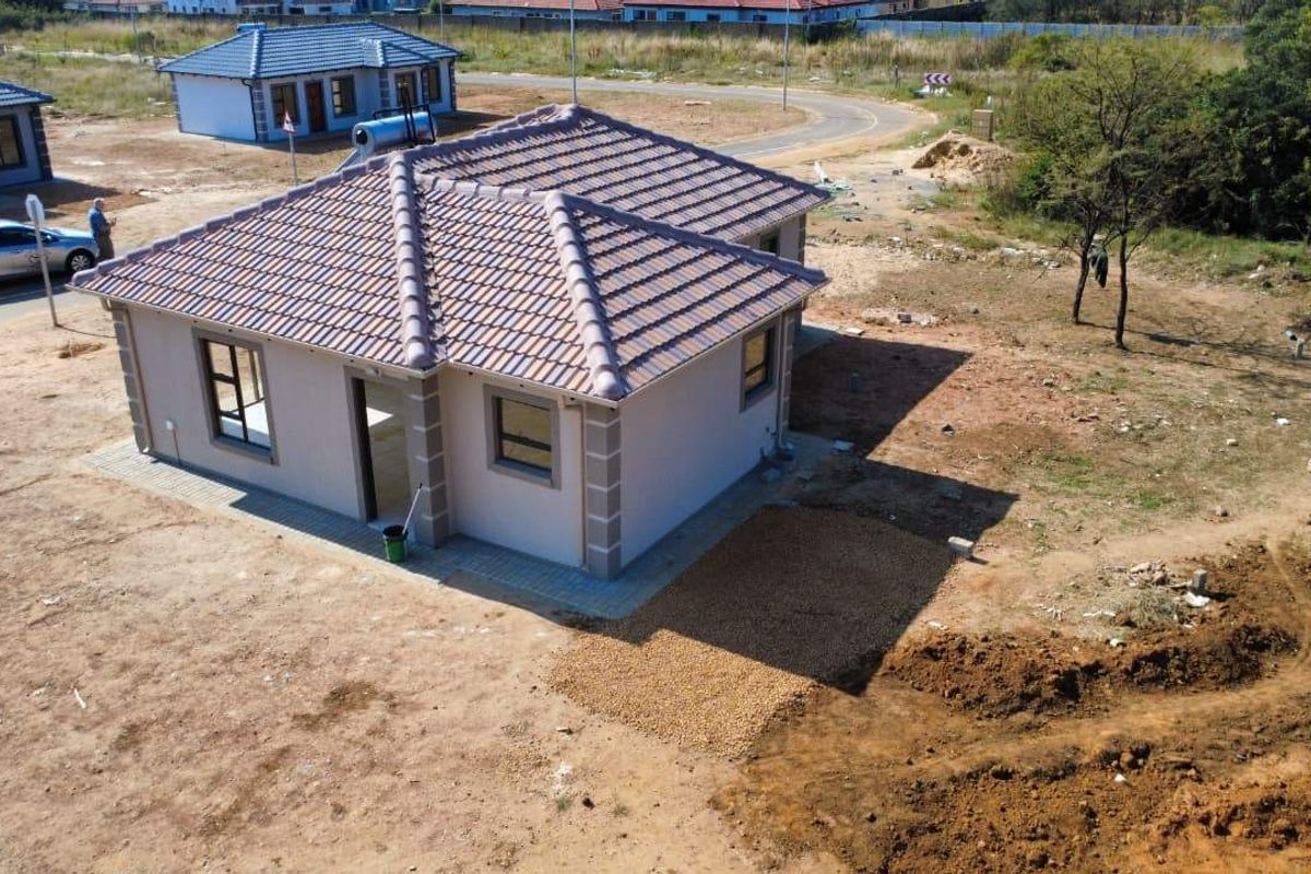 Aerial view of a modern single-story residential house featuring a tiled roof, solar geyser, and paved exterior walkways in a developing estate.
