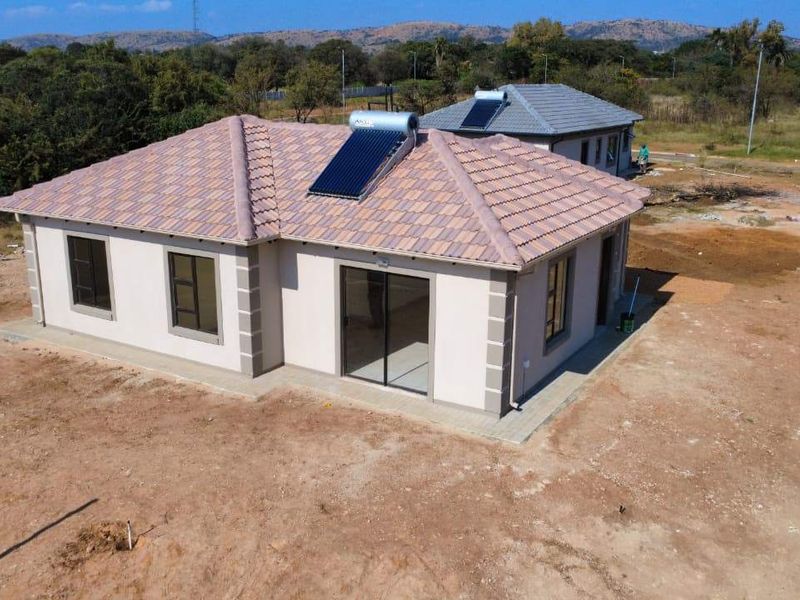 Aerial view of a modern single-story house featuring a tiled roof with solar water heating and surrounding unlandscaped grounds.
