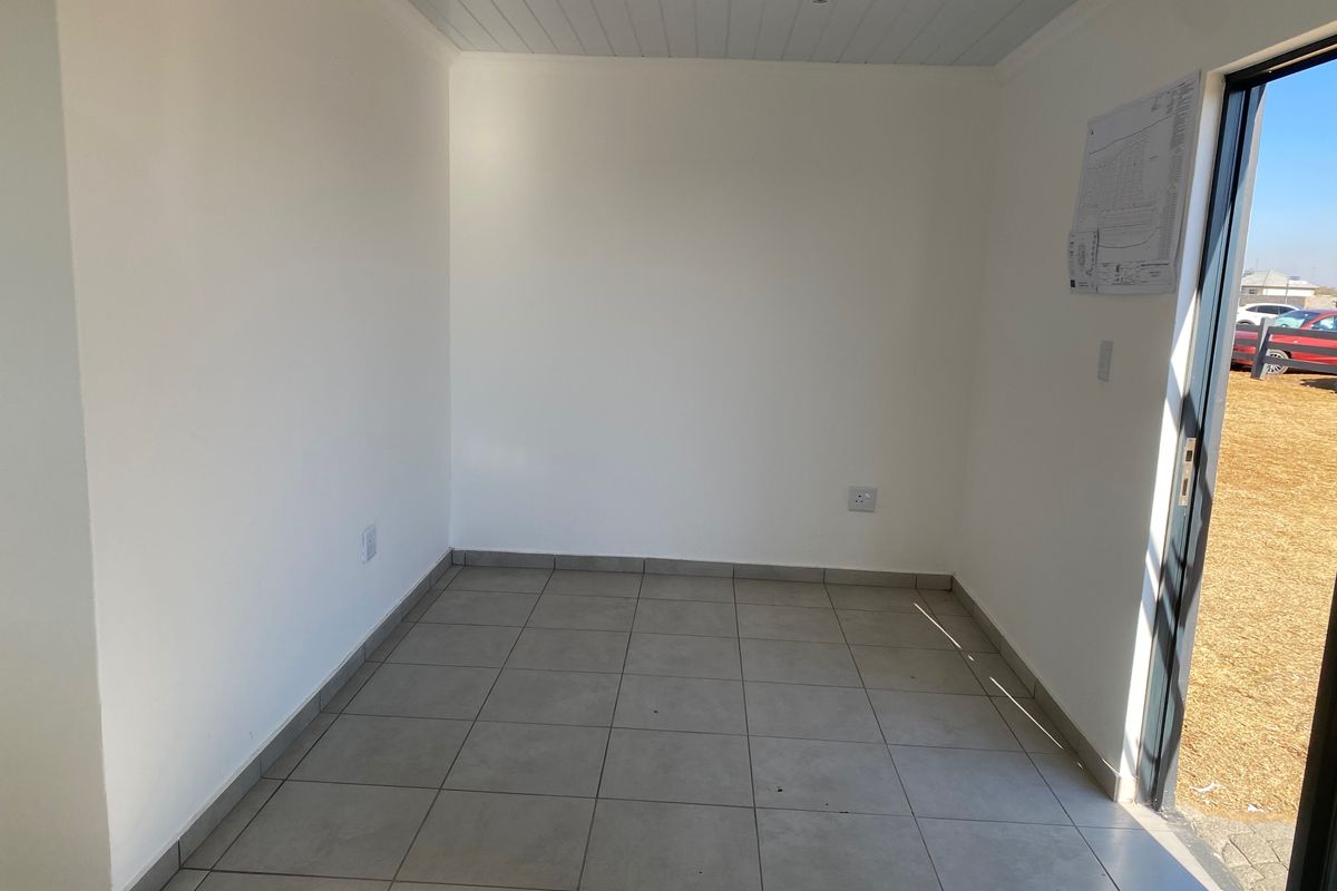 A bright, empty room featuring neutral tiled flooring, recessed ceiling lights, and a sliding glass door providing access to the exterior.