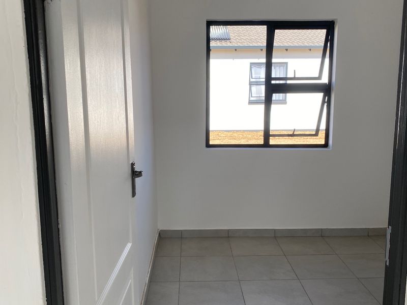 A clean, empty bedroom featuring neutral tiled flooring, white walls, and a modern aluminium window frame, ready for personalization.