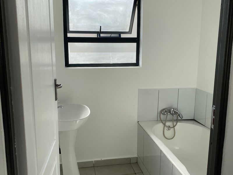 A clean, functional bathroom featuring a pedestal basin, a built-in bathtub with tiled surround, and neutral floor tiling.