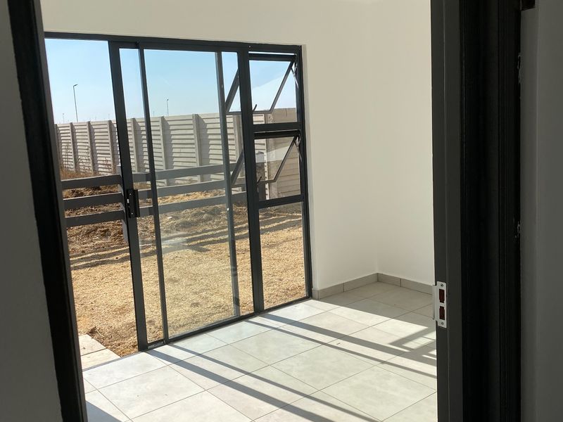 A bright, empty covered patio featuring tiled flooring, recessed ceiling lights, and large sliding glass doors leading to the rear garden area.