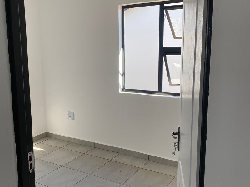 A clean, empty bedroom featuring neutral tiled flooring, white walls, and a modern aluminium window frame, offering a blank canvas for personalization.