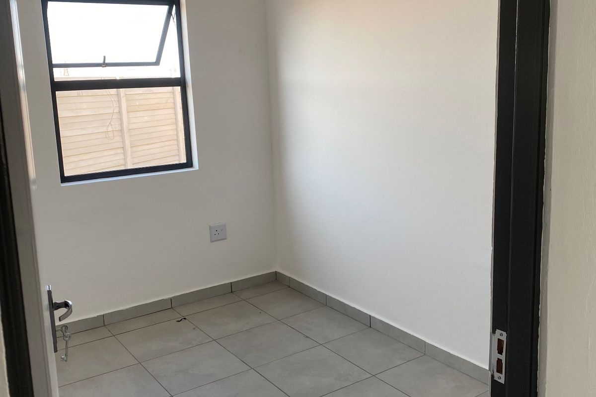 A clean, empty bedroom featuring neutral tiled flooring, a top-hung window, and a white tongue and groove ceiling.