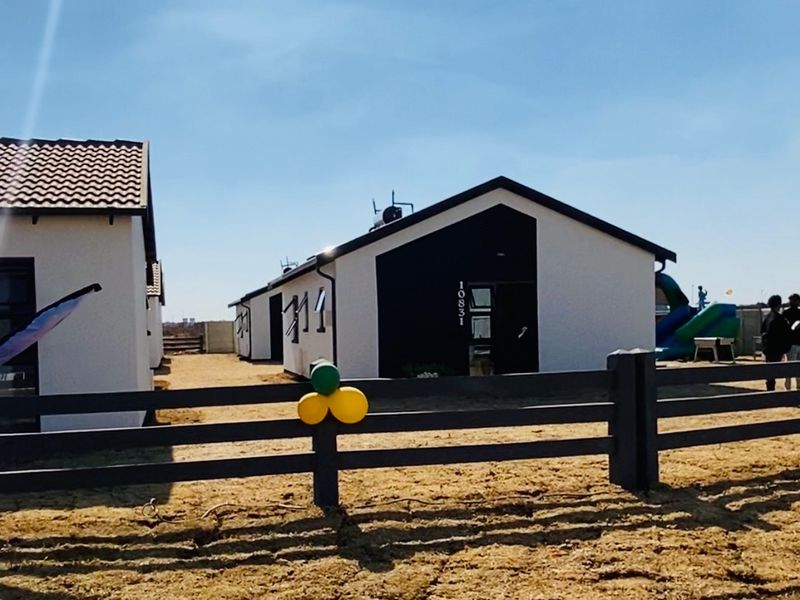 Front view of a modern single-story residential house featuring a dark and white facade, tiled roof, and a perimeter timber fence.