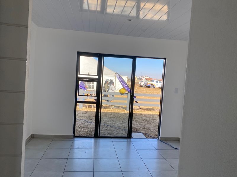 A bright, empty living area featuring neutral tiled flooring and a modern sliding glass door providing direct access to the exterior.
