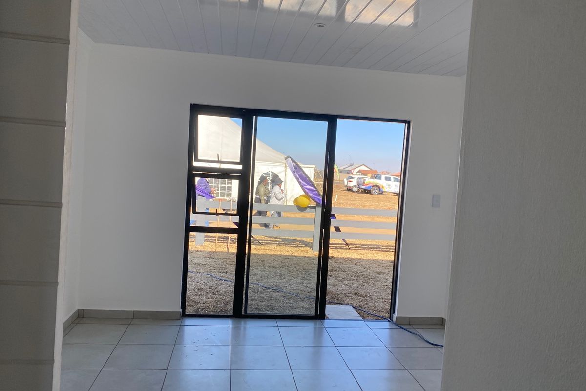A bright, empty living area featuring neutral tiled flooring and a modern sliding glass door providing direct access to the exterior.