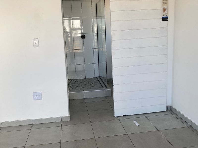 A clean, modern bathroom featuring a glass shower enclosure and a white sliding barn door, set against neutral tiled flooring.