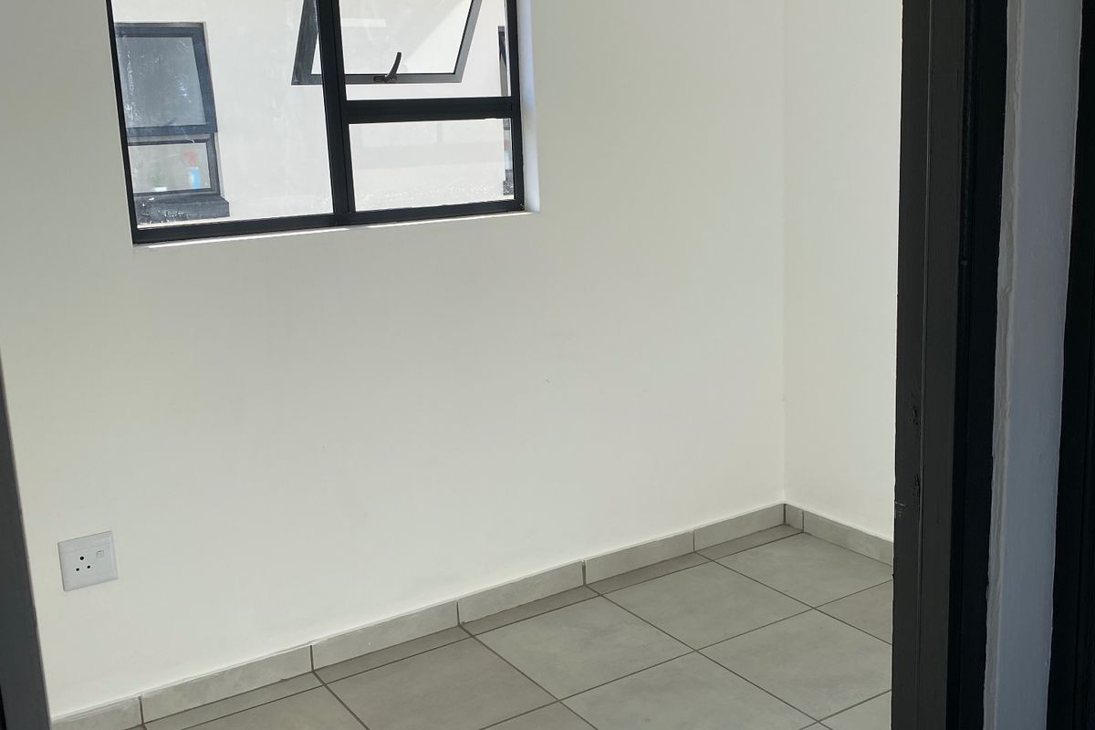 A clean, empty bedroom featuring neutral tiled flooring, a modern aluminium window, and a white tongue and groove ceiling.