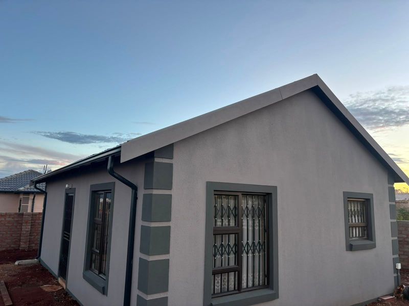 A well-maintained exterior view of the property featuring a clean plastered facade, modern aluminium window frames, and secure metal security gates.