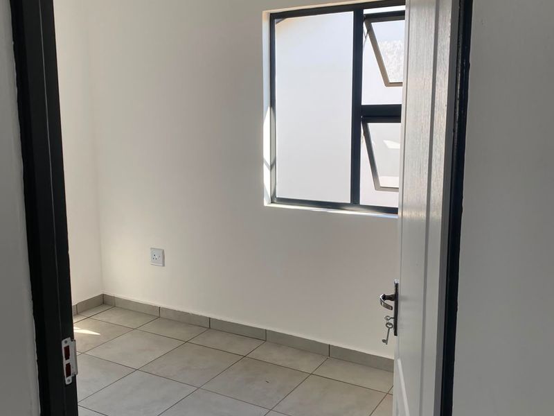 A clean, empty bedroom featuring neutral tiled flooring, white walls, and an aluminium-framed window, providing a blank canvas for interior design.