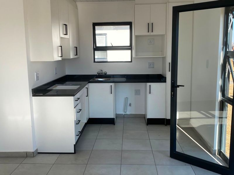 A clean, modern kitchen featuring white cabinetry, black countertops, tiled flooring, and direct access to the outdoors through a glass door.