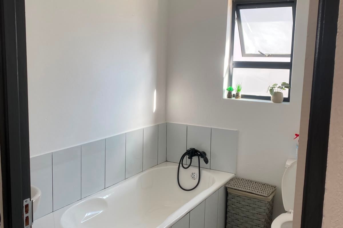 A functional bathroom featuring a bathtub with tiled surround, a toilet, and a window providing natural light.
