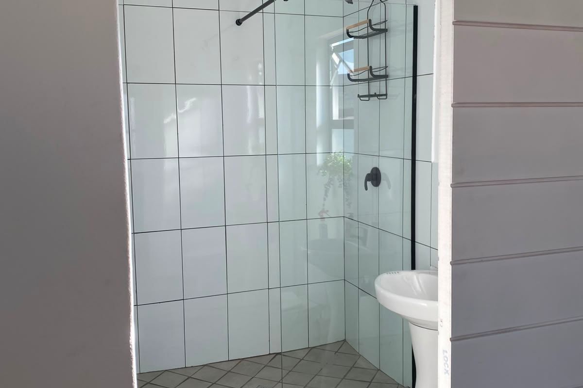 A clean, modern bathroom featuring a walk-in shower with a glass screen, pedestal sink, and white tiled finishes.