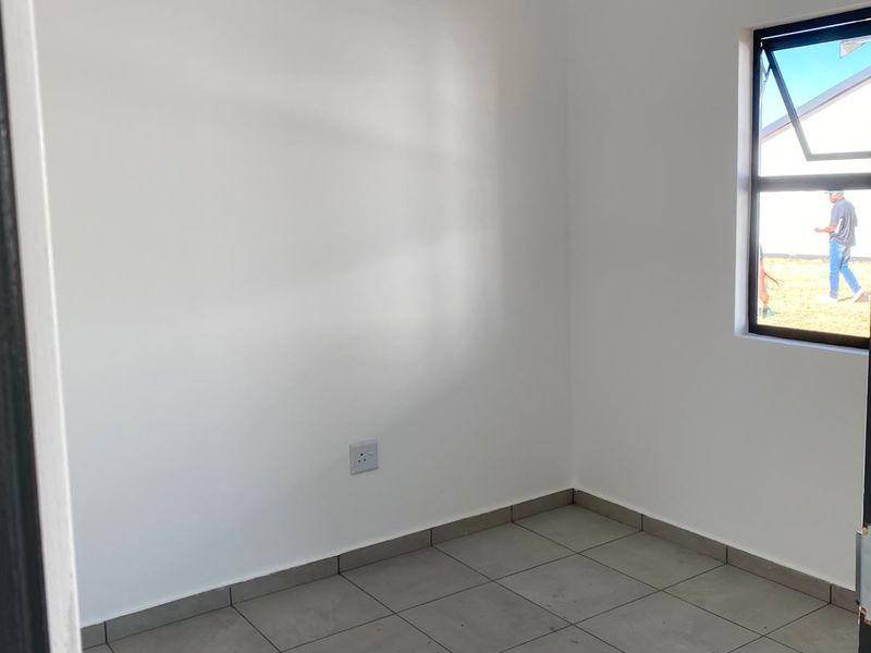 A clean, empty bedroom featuring neutral tiled flooring, white walls, and a modern tongue and groove ceiling with an aluminium window.