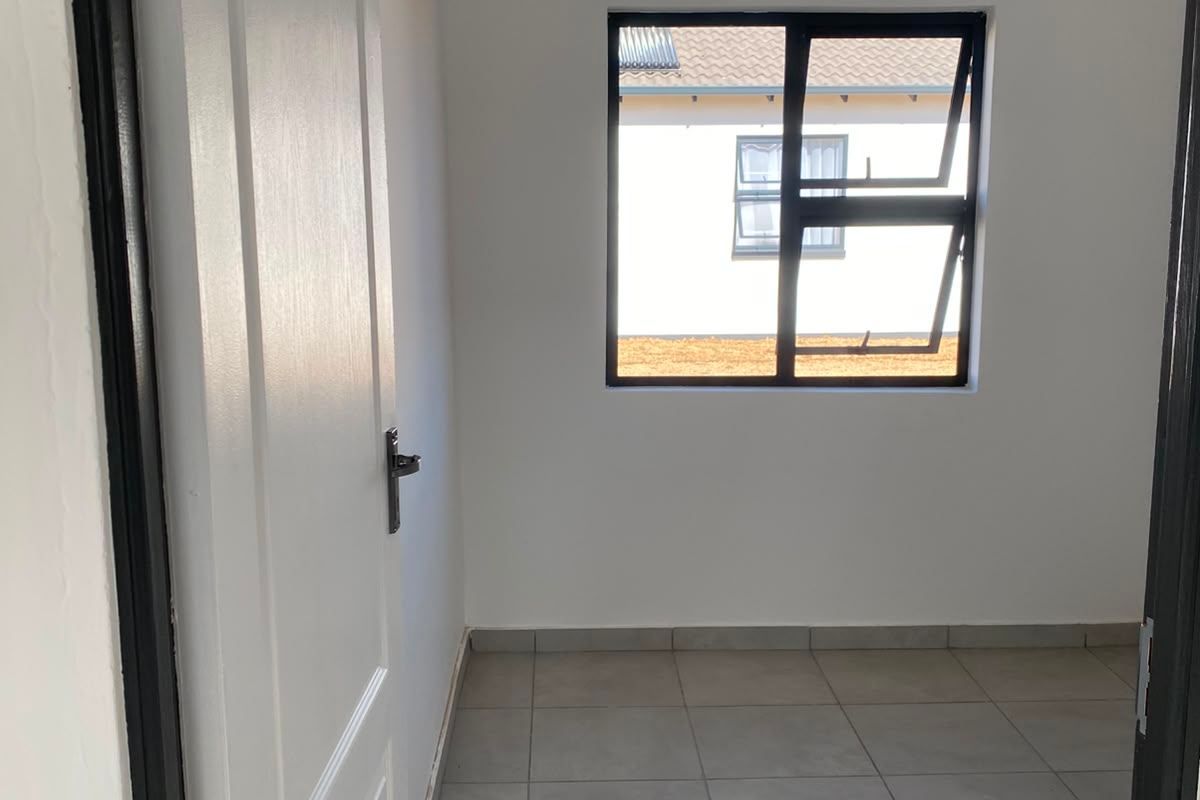 A clean, empty bedroom featuring neutral tiled flooring, a modern aluminium window, and a white panelled door.