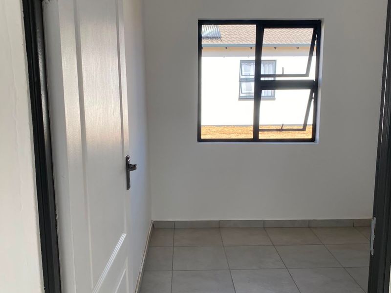 A clean, empty bedroom featuring neutral tiled flooring, a modern aluminium window, and a white panelled door.