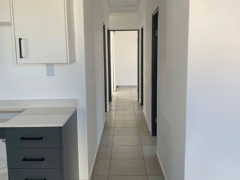 A clean, modern hallway featuring neutral tiled flooring, white walls, and a sleek laminate ceiling, leading to multiple internal rooms.